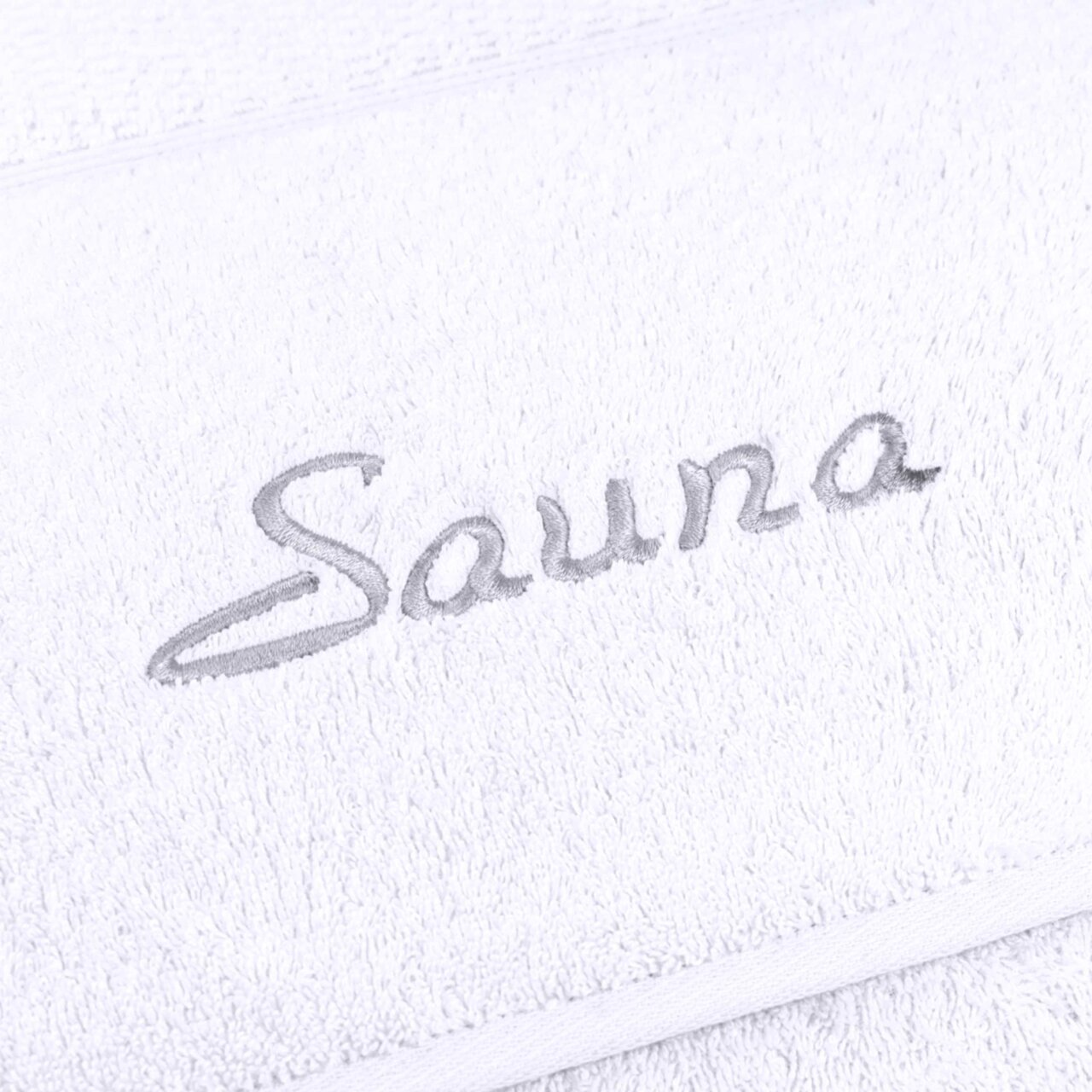 Nahaufnahme eines weißen Saunatuchs mit grauer Stickerei des Wortes 'Sauna'.