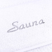 Nahaufnahme eines weißen Saunatuchs mit grauer Stickerei des Wortes 'Sauna'.