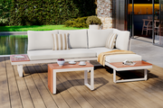 Moderne Gartenlounge mit weißem Polster und Holztischen, seitliche Perspektive, im Freien auf einer Terrasse mit Blick auf den Garten.