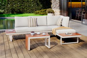 Moderne Gartenlounge mit weißem Polster und Holztischen, seitliche Perspektive, im Freien auf einer Terrasse mit Blick auf den Garten.