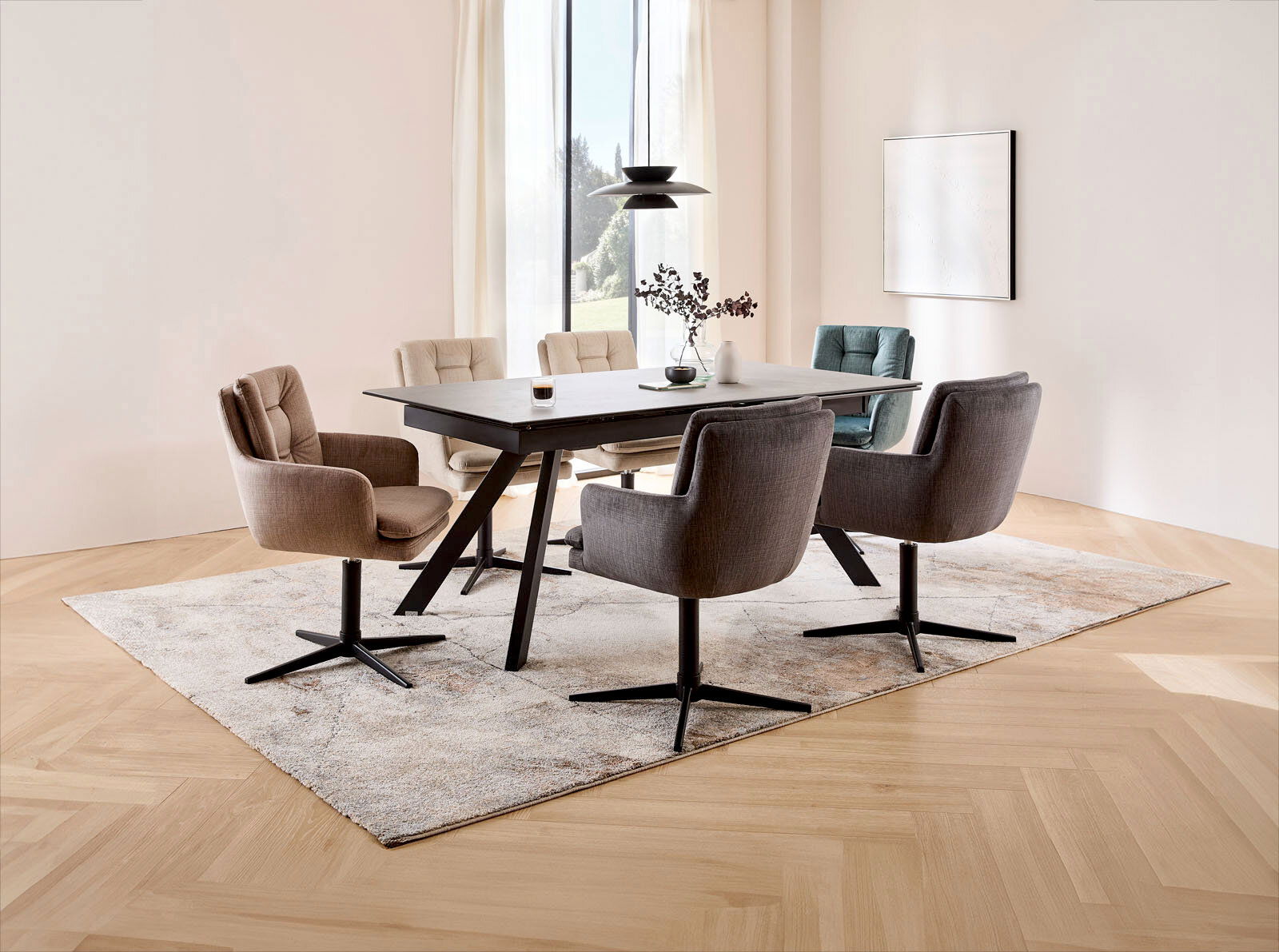 Moderner Essbereich mit einem rechteckigen Esstisch und sechs gepolsterten Armlehnstühlen in verschiedenen Farben, auf einem Teppich in einem hellen Raum mit großen Fenstern. Perspektive von schräg oben.