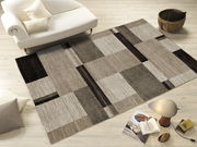 Moderner Teppich in Beige- und Brauntönen mit geometrischem Muster, auf hellem Holzboden neben einem weißen Sofa und einem Beistelltisch mit Lampe, aus der Vogelperspektive.