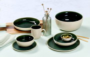 Vielseitiges Geschirrset in elegantem Dunkelgrün und Creme, bestehend aus Tassen, Tellern und Schalen, auf einem Tisch arrangiert. Seitliche Perspektive.