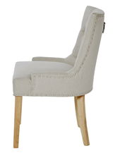 Seitenansicht eines eleganten, beige gepolsterten Stuhls mit Nietenverzierung und Holzbeinen.
