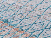 Nahaufnahme eines Designer-Teppichs mit einem modernen, geometrischen Muster in Blau- und Beigetönen, schräg von oben fotografiert.