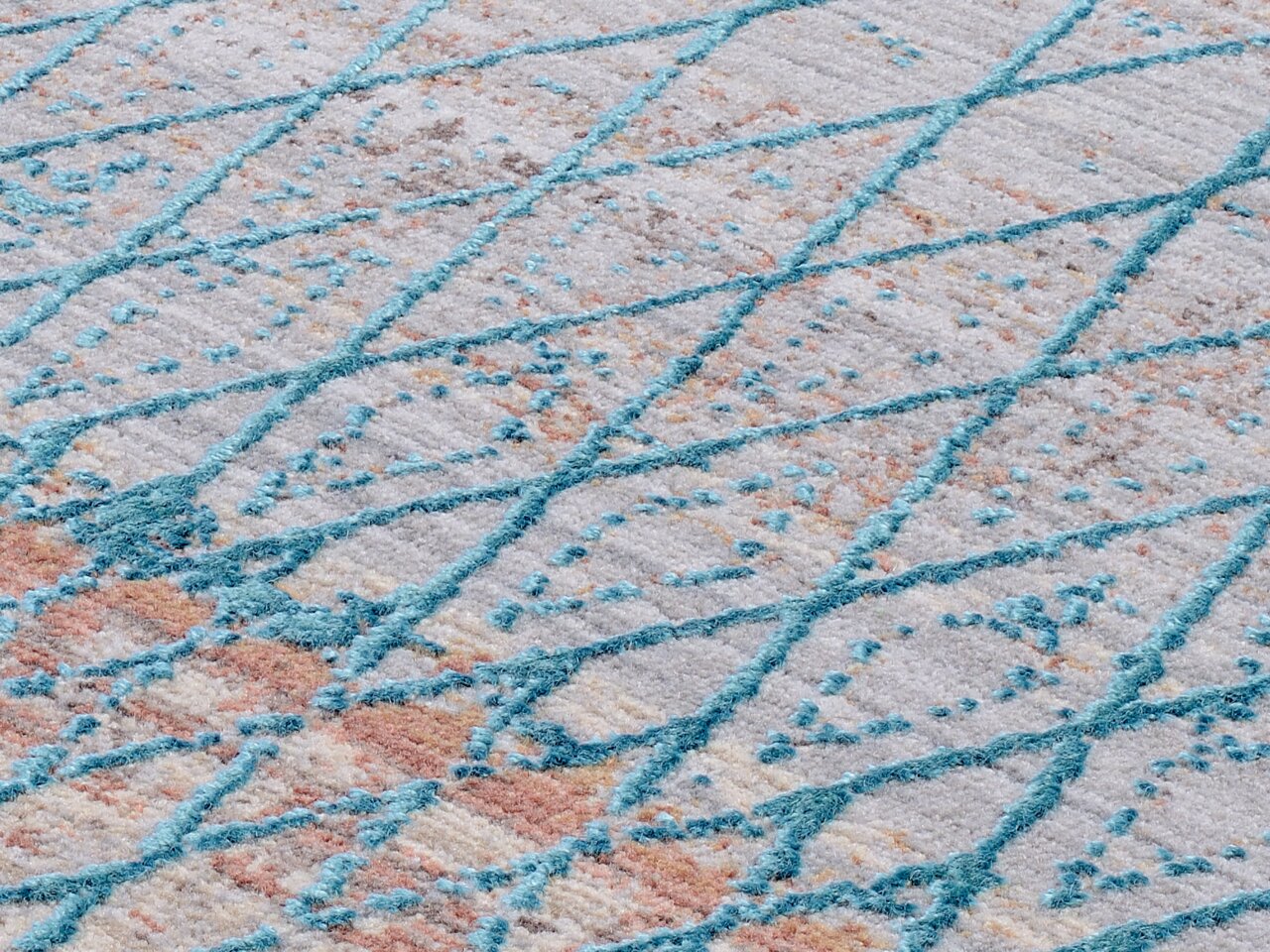 Nahaufnahme eines Designer-Teppichs mit einem modernen, geometrischen Muster in Blau- und Beigetönen, schräg von oben fotografiert.