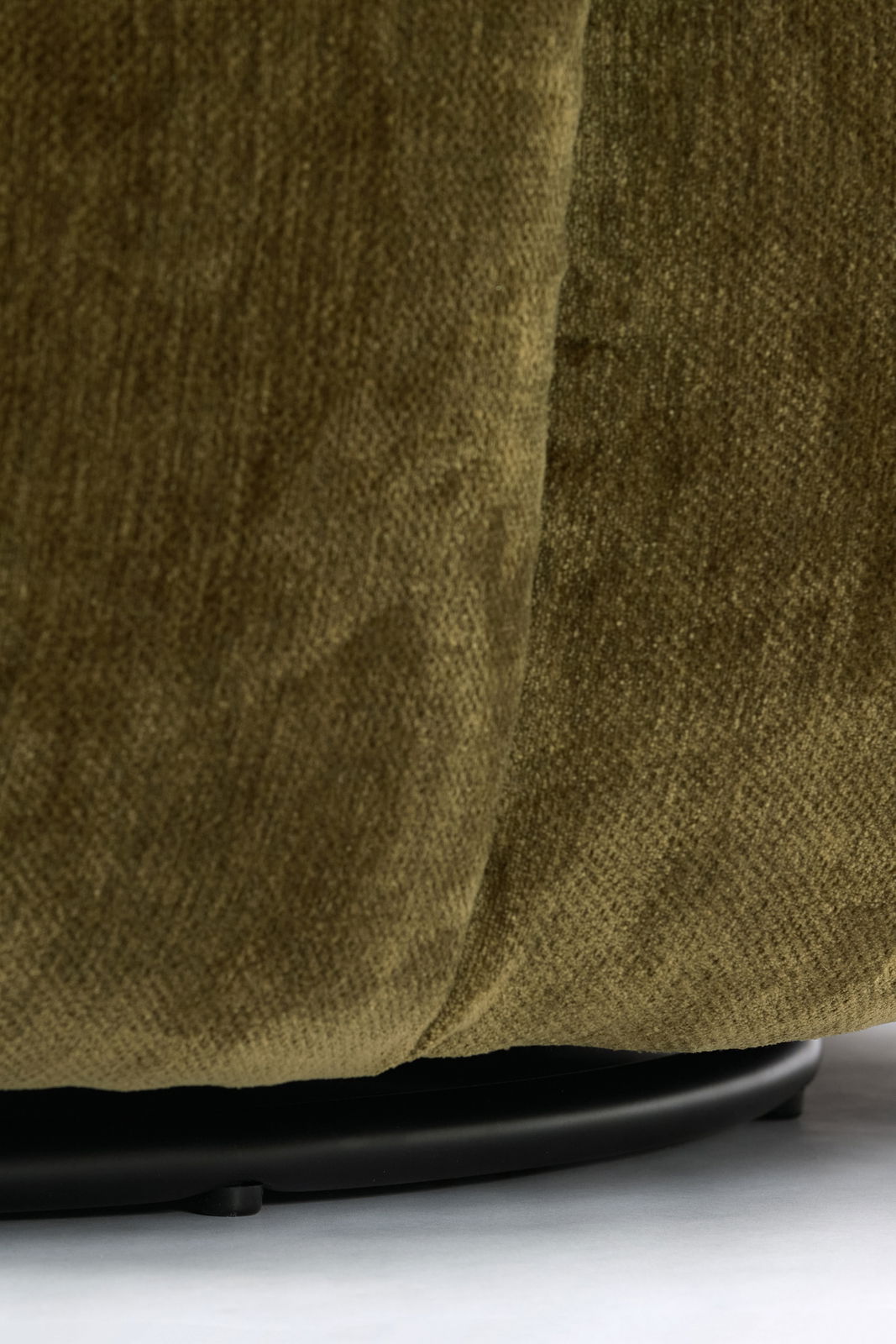 Nahaufnahme eines grünen Sessels mit Stoffbezug, Fokus auf die untere Kante und den schwarzen Sockel.