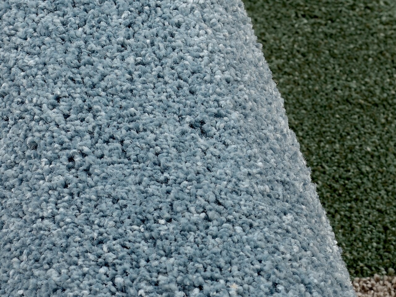 Nahaufnahme eines blauen Uni-Teppichs mit weicher, flauschiger Textur, von der Seite betrachtet.