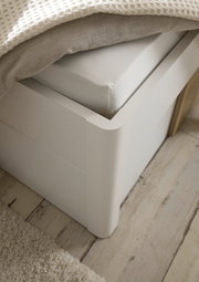 Nahaufnahme einer weißen Bettrahmenecke mit Matratze und Decke, aus der Perspektive von oben.