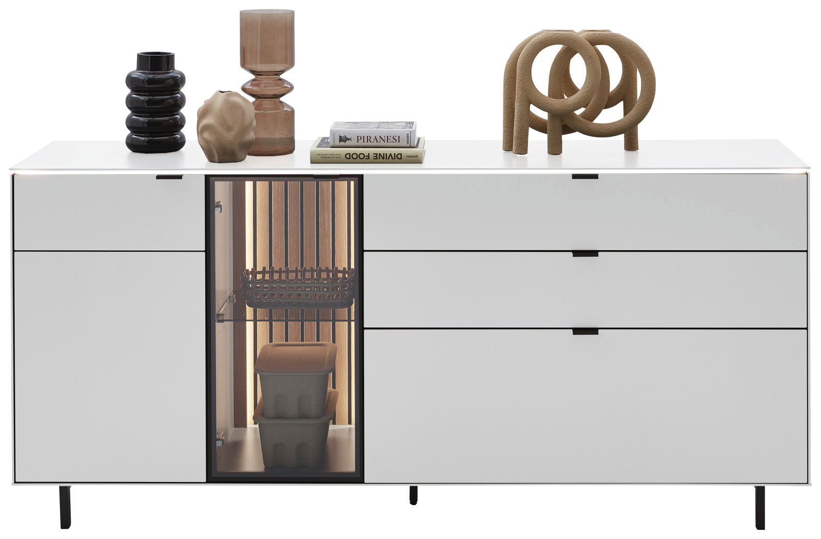 Modernes weißes Sideboard mit dekorativen Objekten auf der Oberseite, darunter Vasen und Bücher, sowie ein beleuchtetes Fach mit Körben und Behältern, frontal betrachtet.
