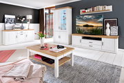 Helles Wohnzimmer-Set im Landhausstil mit weißer Holzoptik und Eichefarben-Absetzungen: Sideboard links, hohe Vitrine mittig, TV-Lowboard rechts und Couchtisch im Vordergrund; Perspektive: frontale Weitwinkelansicht leicht von links.
