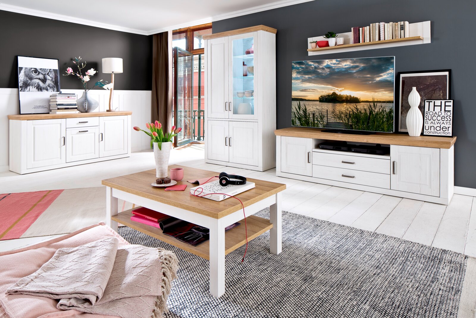 Landscape Tv-kast BREGENZ Lichte woonkamerset in landhuisstijl met een witte houtlook en eikenhouten accenten: dressoir links, hoge vitrinekast in het midden, tv-kast rechts en salontafel op de voorgrond; perspectief: frontale groothoekopname, licht van links.