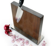 Magnet-Messerblock aus Esche mit einem Messer, das daran haftet, und geschnittenen roten Zwiebeln auf einer weißen Oberfläche, seitliche Perspektive.