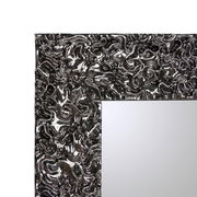 Nahaufnahme eines Spiegels mit einem kunstvoll strukturierten, glänzenden Rahmen in Silberoptik, perspektivisch von der Seite aufgenommen.