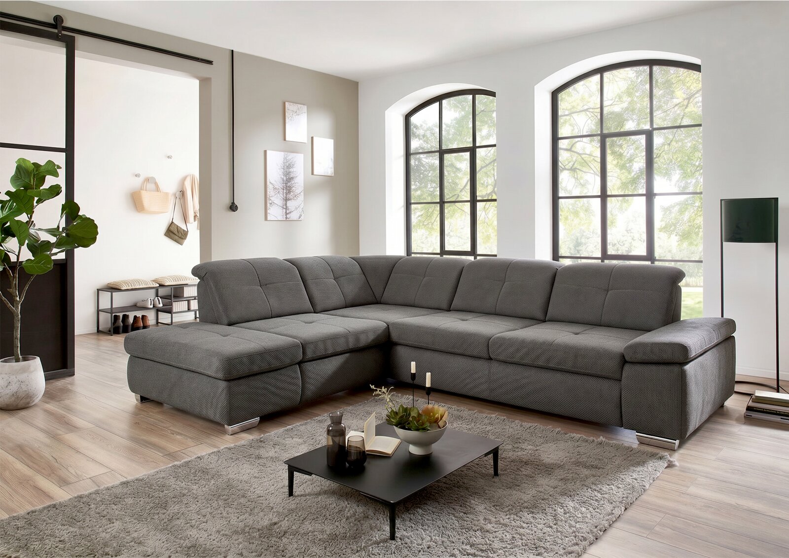 Beldomo Style Ecksofa AUSTIN Graues, modernes U-förmiges Wohnlandschaft-Ecksofa mit breiter Ottomane und gepolsterter Rückenlehne in hellem Wohnzimmer; Perspektive: frontale leicht schräge Ansicht von links.