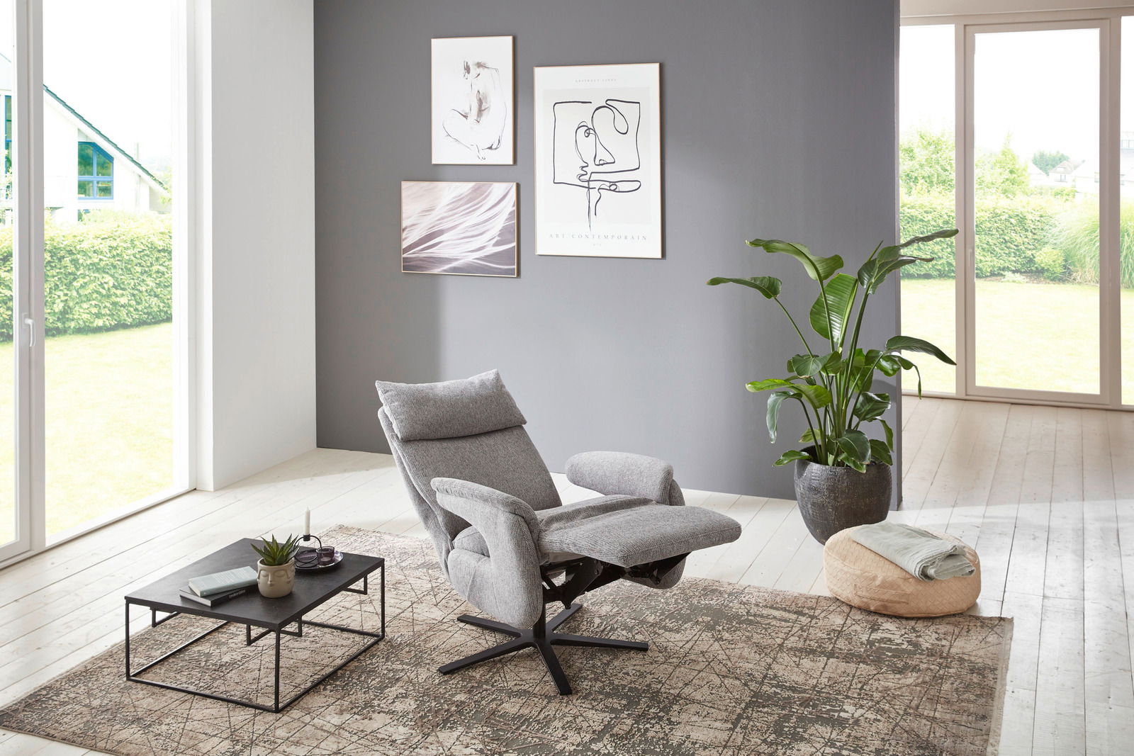 Moderner grauer Fernsehsessel in einem hellen Wohnzimmer, seitliche Perspektive.