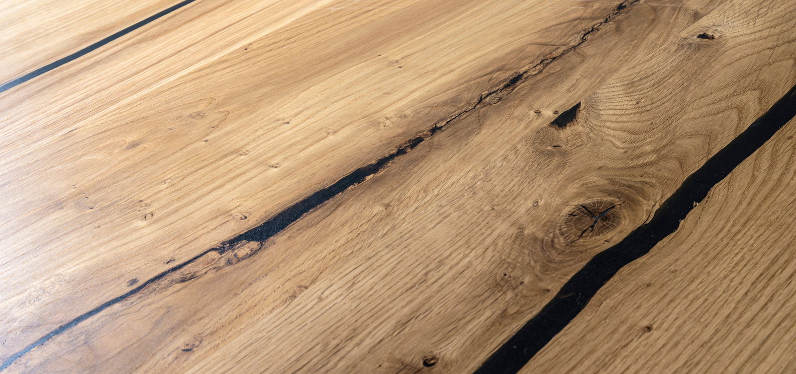 Nahaufnahme der Holzoberfläche eines Esstisches mit natürlichen Maserungen und Rissen, aus einer schrägen Perspektive aufgenommen.
