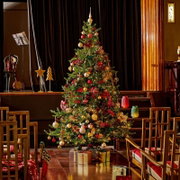 Vooraanzicht van een rijk versierde kerstboom met warme lichtjes, rode en gouden ornamenten en cadeaus in een sfeervolle theaterzaal
