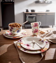 Frontalansicht eines eleganten Geschirrsets mit floralen Mustern, bestehend aus Tellern, Tassen und Schalen, auf einem Holztisch in einer modernen Küche.