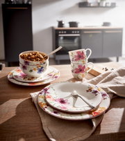 Frontalansicht eines eleganten Geschirrsets mit floralen Mustern, bestehend aus Tellern, Tassen und Schalen, auf einem Holztisch in einer modernen Küche.