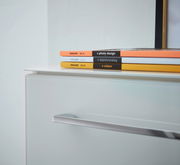 Nahaufnahme eines weißen Aktenschranks mit modernen Griffen, darauf liegen bunte Zeitschriften. Perspektive von schräg oben.