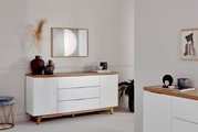 Weißes Sideboard mit Holzoberfläche, dekoriert mit Vasen und Kunstwerken, aus seitlicher Perspektive fotografiert.