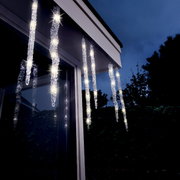 LED-ijspegellampjes met knipperend effect, opgehangen aan een dakrand bij schemering, van onderaf gezien.