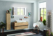 Moderne Badkombination mit Holzoptik, bestehend aus einem Waschtisch mit Unterschrank, einem hohen Schrank und einem beleuchteten Spiegel, seitliche Perspektive.