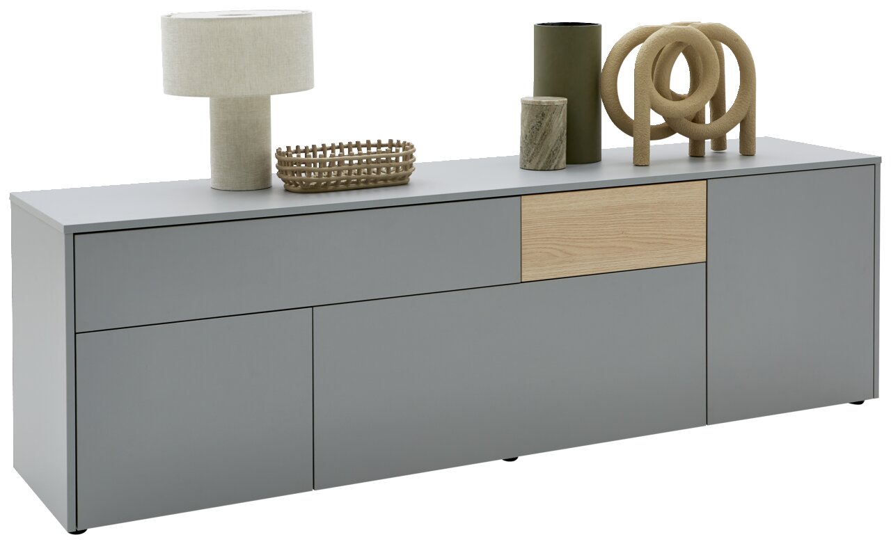 Voleo TV-Lowboard NAOMI Modernes TV-Lowboard in Grau mit Holzakzent, dekoriert mit einer Tischlampe, einem Korb und weiteren Accessoires, seitliche Perspektive.