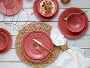 Draufsicht auf ein rosa/korallfarbenes Geschirr-Set mit geprägtem Mandala-Ornament (Teller und Schalen) auf weißem Holztisch, dekoriert mit goldfarbenem Besteck, geflochtenem Platzset und weißer Serviette.