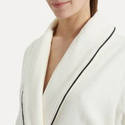 Nahaufnahme eines weißen Bademantels mit Schalkragen und schwarzer Paspelierung, getragen von einer Person.