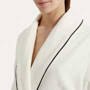 Nahaufnahme eines weißen Bademantels mit Schalkragen und schwarzer Paspelierung, getragen von einer Person.