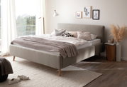 Modernes Polsterbett in einem hellen Schlafzimmer, seitliche Perspektive, mit dekorativen Kissen und Decken, umgeben von minimalistischer Einrichtung.