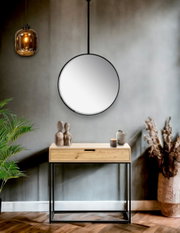Runder Wandspiegel mit schwarzem Metallrahmen und Aufhängung über einer Holz-Konsole in modernem Flur, Frontansicht