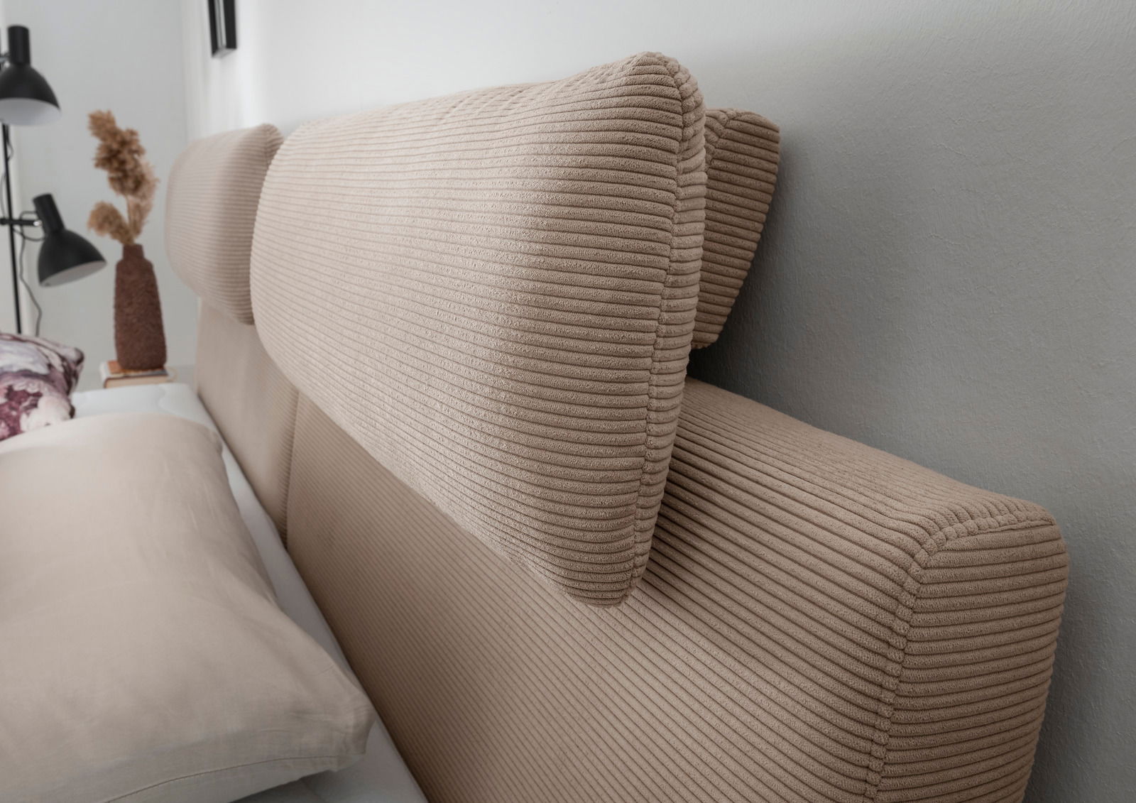 Nahaufnahme eines beigen Boxspringbett-Kopfteil mit gerippter Textur, seitliche Perspektive