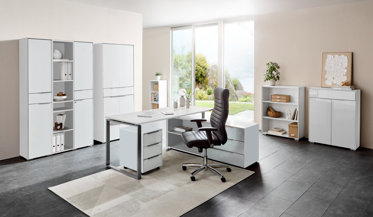 Moderne kantoormeubelcombinatie in een lichte ruimte met een groot raam. Op de voorgrond een hoekbureau met een rolcontainer en een ergonomische bureaustoel. Op de achtergrond staan verschillende archiefkasten en rekken. Aanzicht van voren.