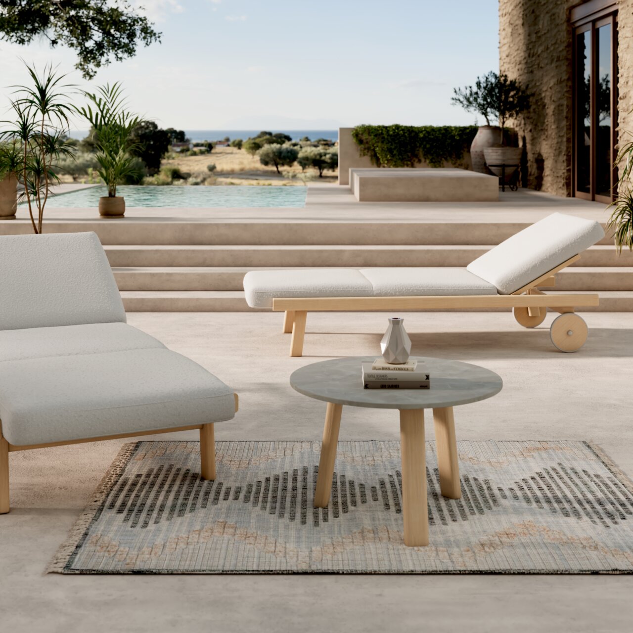 Dieter Knoll Sonnenliege MARI Moderne Gartenlounge mit Sonnenliege und rundem Loungetisch auf Terrasse mit Blick auf Pool und Landschaft, seitliche Perspektive.