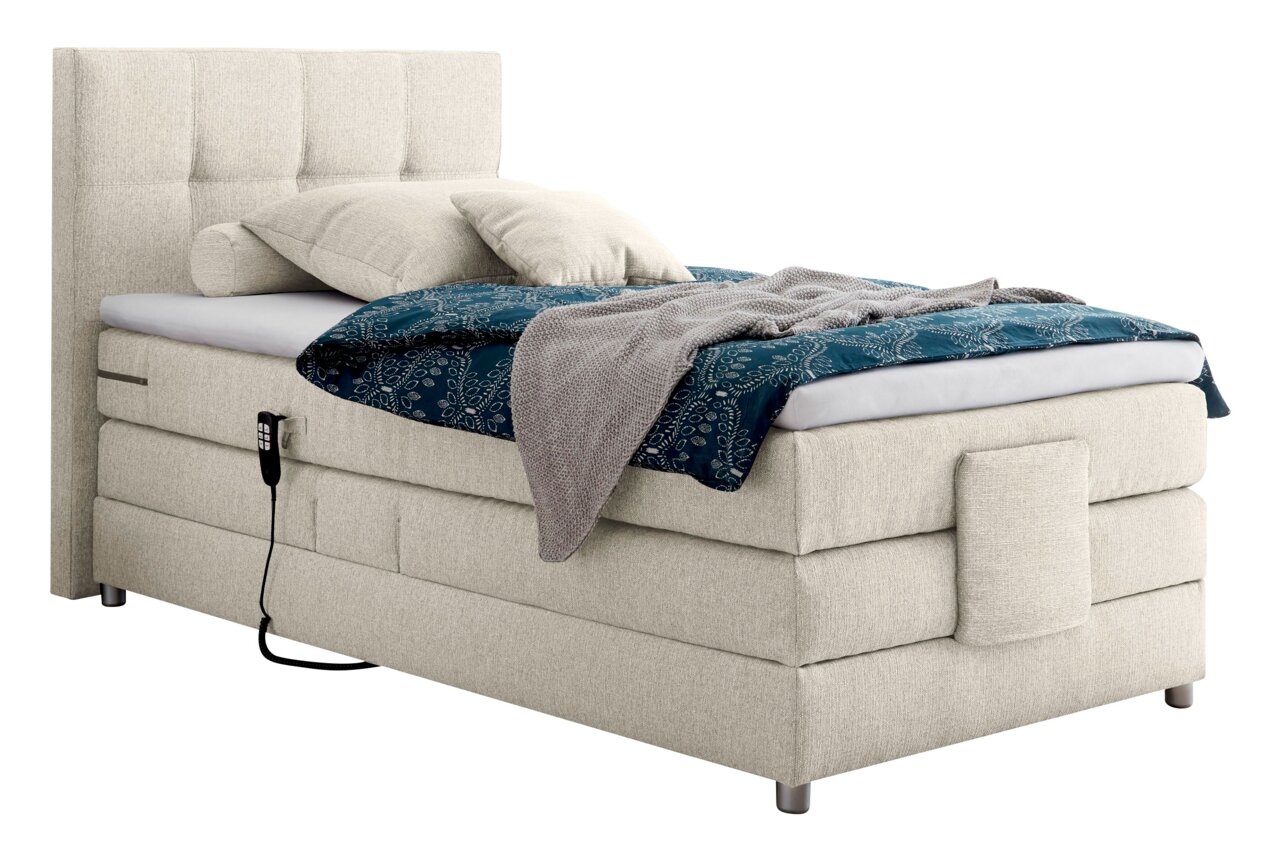 Boxspringbed in zijaanzicht met een beige stoffen bekleding, hoofdeinde, blauwe deken en kussens.