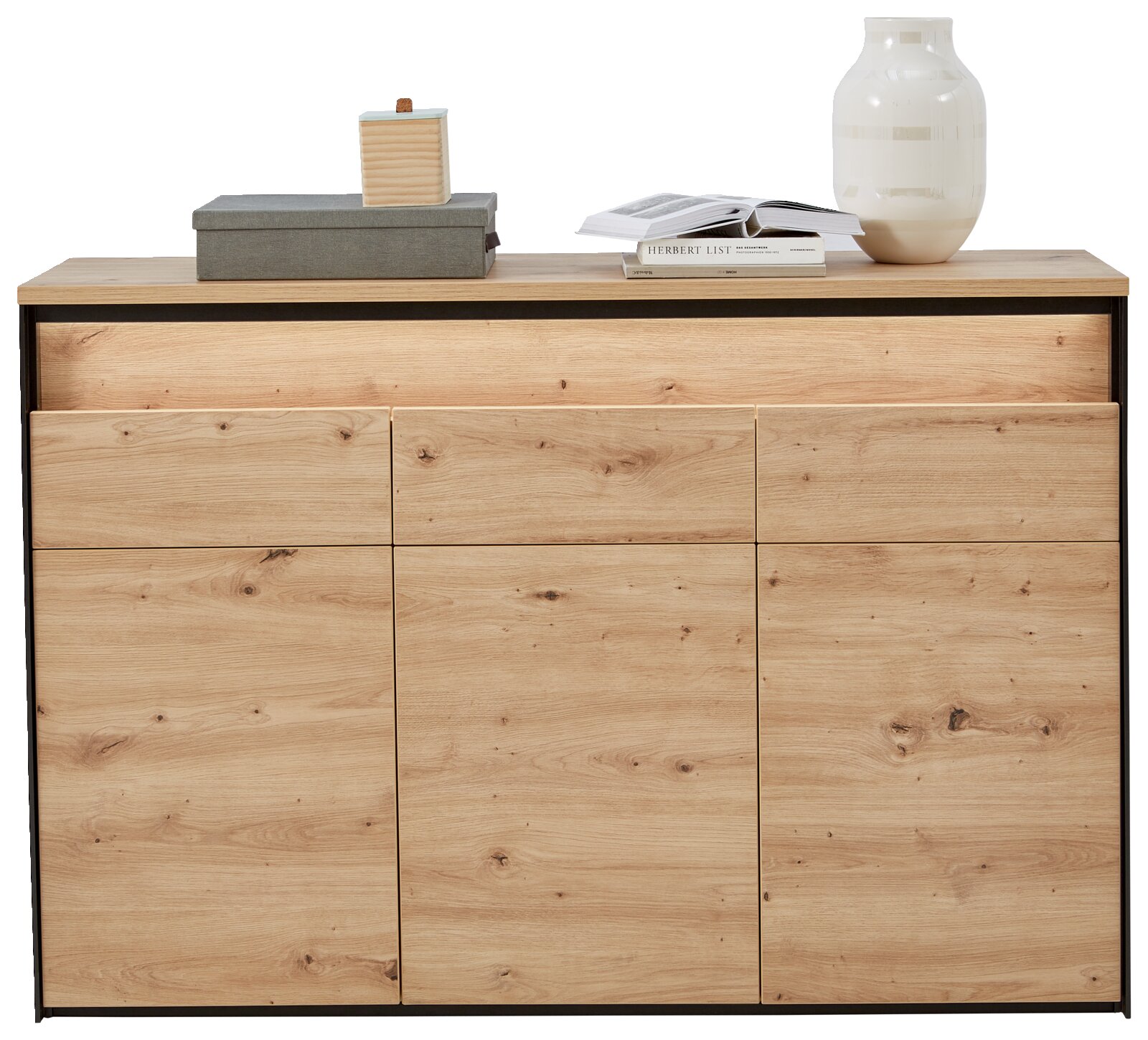 Vooraanzicht van een modern dressoir van licht hout met drie lades en twee deuren, versierd met een vaas, een boek en een doos op het blad.