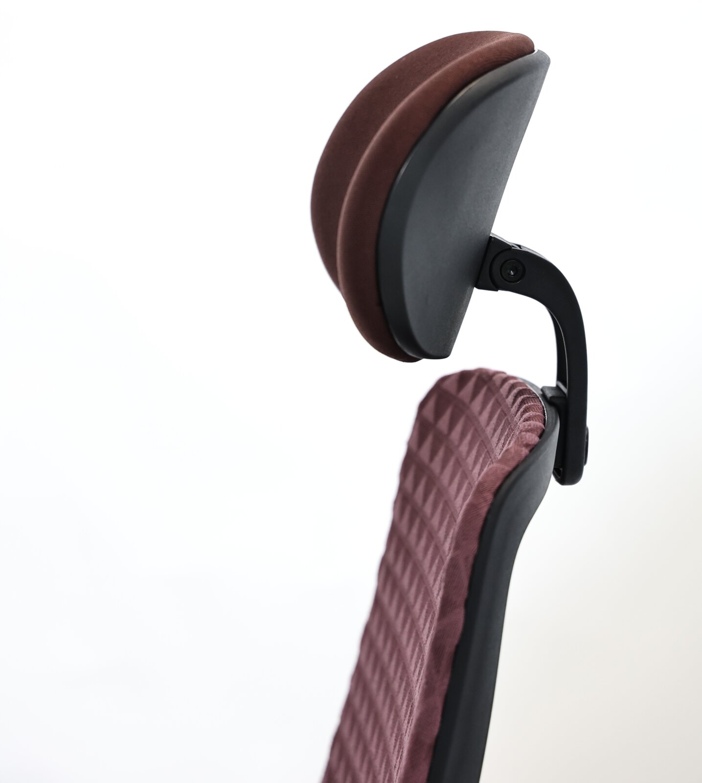Nahaufnahme eines ergonomischen Drehstuhls mit gepolsterter Kopfstütze und rautenförmigem Muster auf der Rückenlehne, seitliche Perspektive.