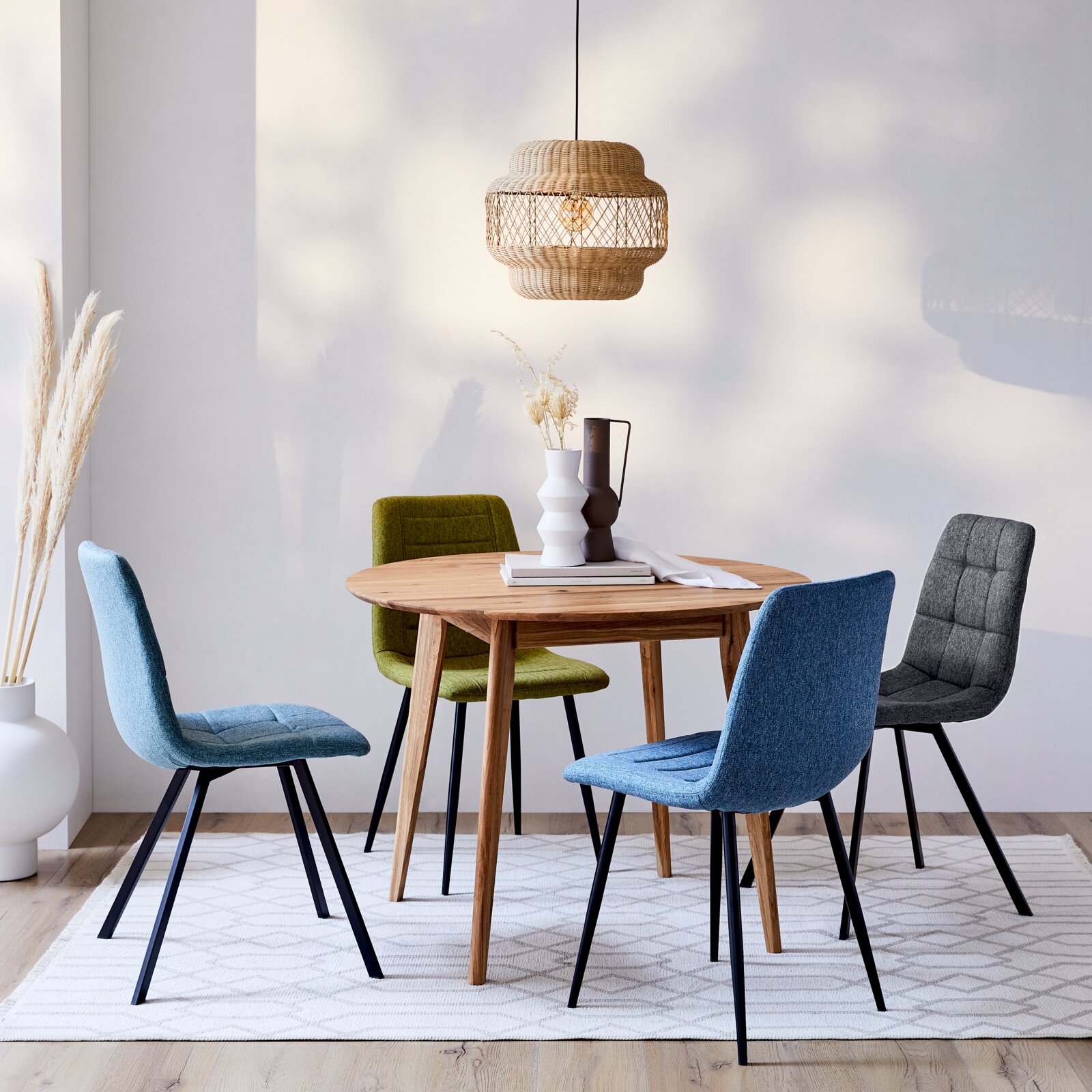 Runder Esstisch aus Holz mit vier bunten Stühlen, aus der Perspektive leicht von oben betrachtet, in einem modernen Esszimmer mit hängender Lampe und Dekoration.