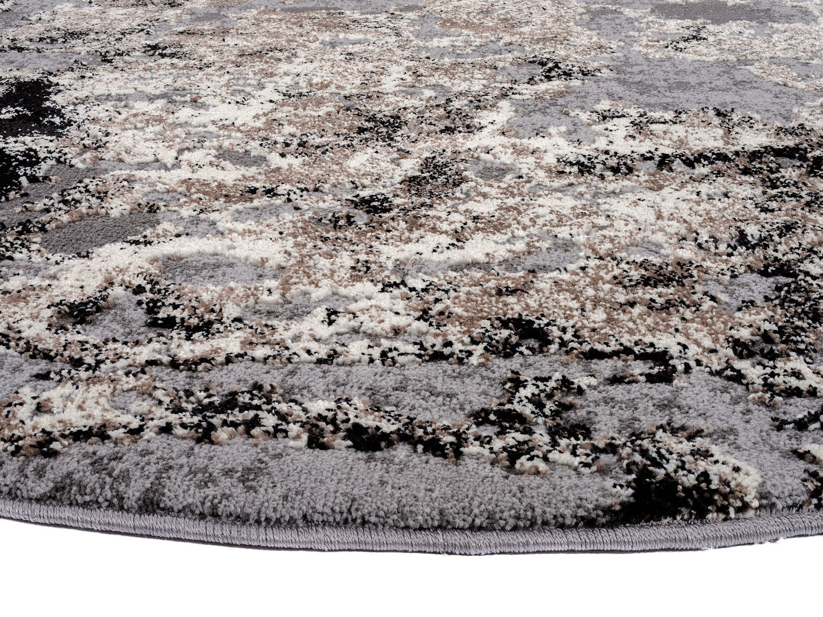 Nahaufnahme eines Designer-Teppichs mit abstraktem Muster in Grau-, Beige- und Schwarztönen, perspektivisch von der Seite aufgenommen.