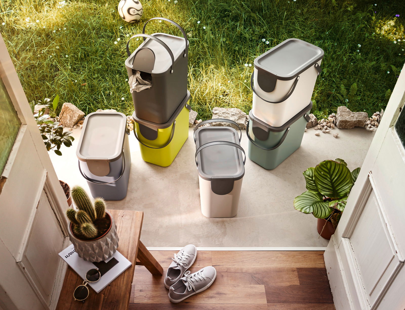 Recycling-Müllsysteme in verschiedenen Farben und Größen, auf einer Terrasse mit Blick von oben, umgeben von Pflanzen und einem Fußball.