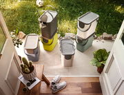 Recycling-Müllsysteme in verschiedenen Farben und Größen, auf einer Terrasse mit Blick von oben, umgeben von Pflanzen und einem Fußball.