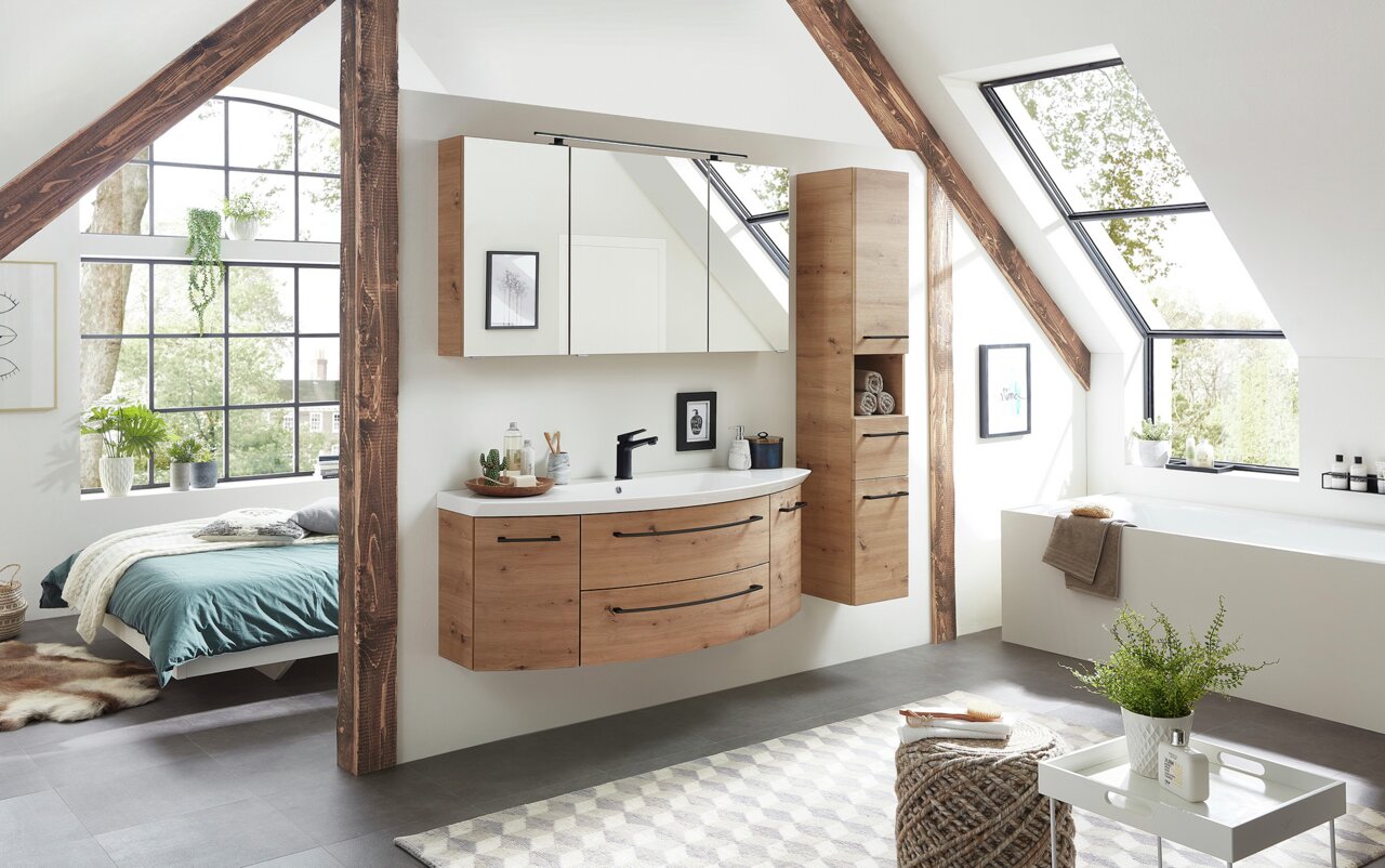 Moderner Hochschrank aus Holz in einem stilvollen Badezimmer mit Dachschräge, neben einem Waschtisch und Spiegeln, mit Blick auf ein großes Fenster.