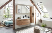 Moderne houten hoge kast in een stijlvolle badkamer met schuin dak, naast een wastafel en spiegels, met uitzicht op een groot raam.