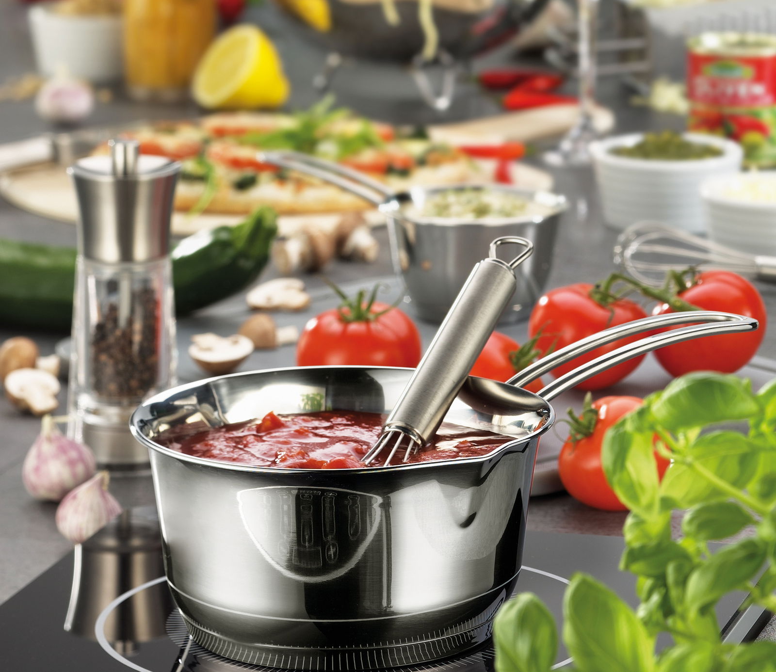 Stiehltopf COOK 1,5L aus Edelstahl mit Soße gefüllt, auf einem Herd stehend, umgeben von frischen Zutaten wie Tomaten und Kräutern, seitliche Perspektive.