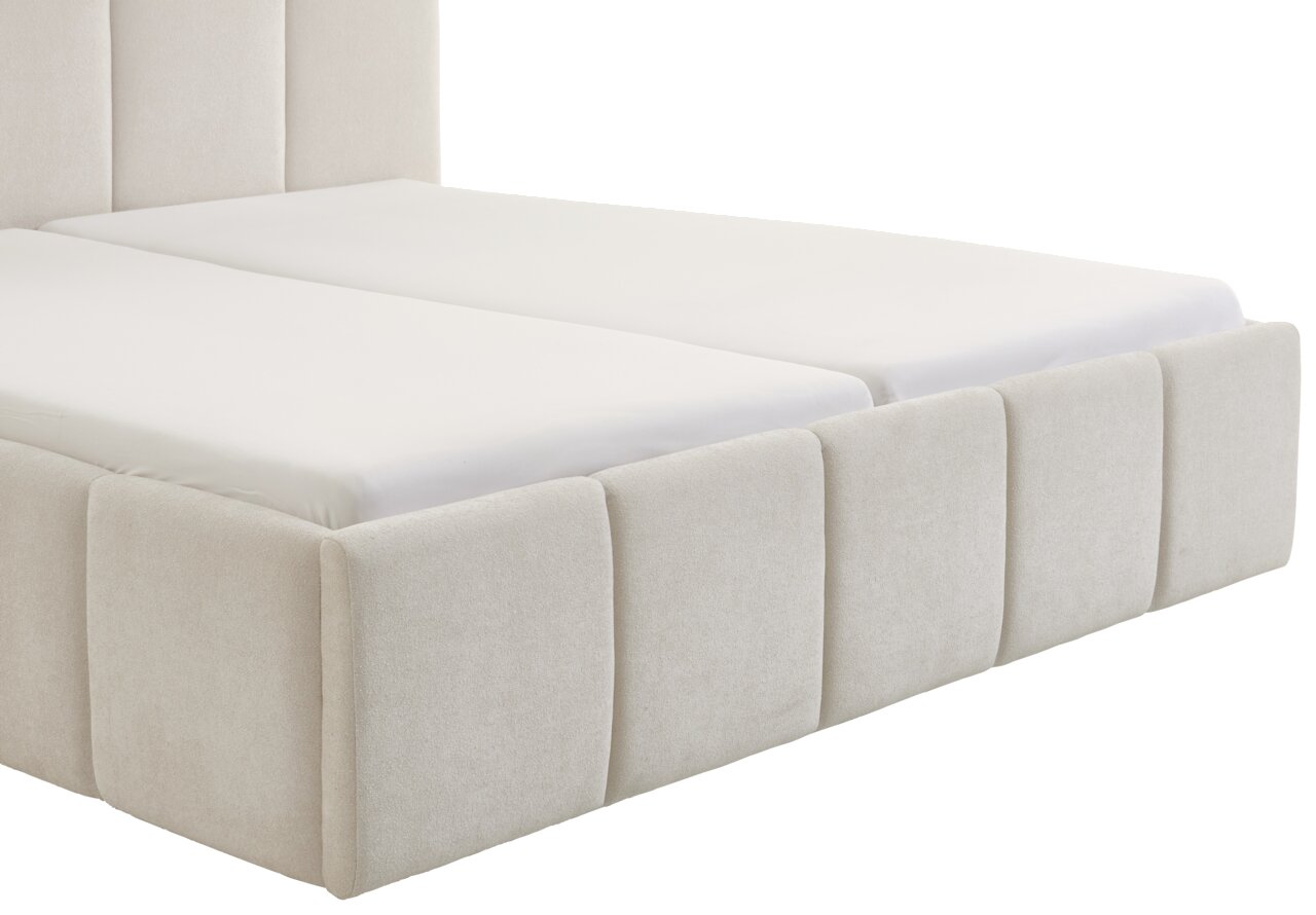 Zijaanzicht van een modern gestoffeerd bed met een lichte stoffen bekleding en een gestoffeerd hoofdeinde.