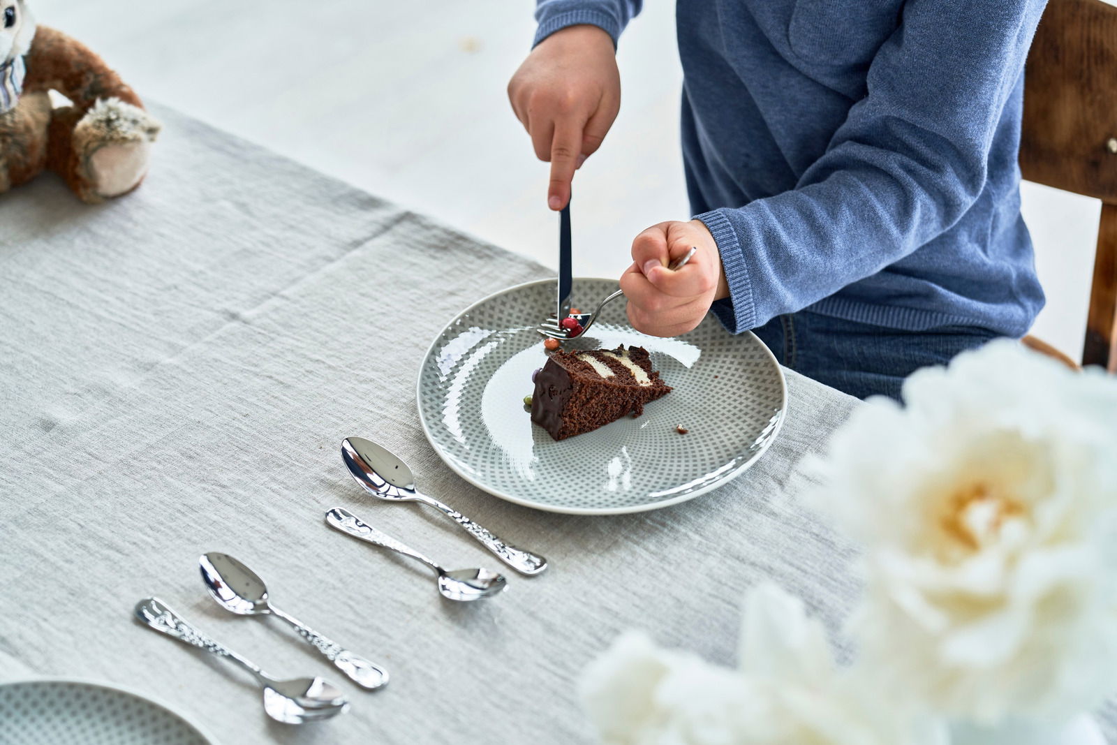Ein Kind schneidet ein Stück Schokoladenkuchen mit einem Kinderbesteck auf einem gedeckten Tisch. Perspektive von oben.