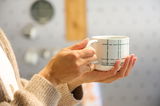 Nahaufnahme einer Hand, die einen Becher mit Henkel und geometrischem Muster hält.